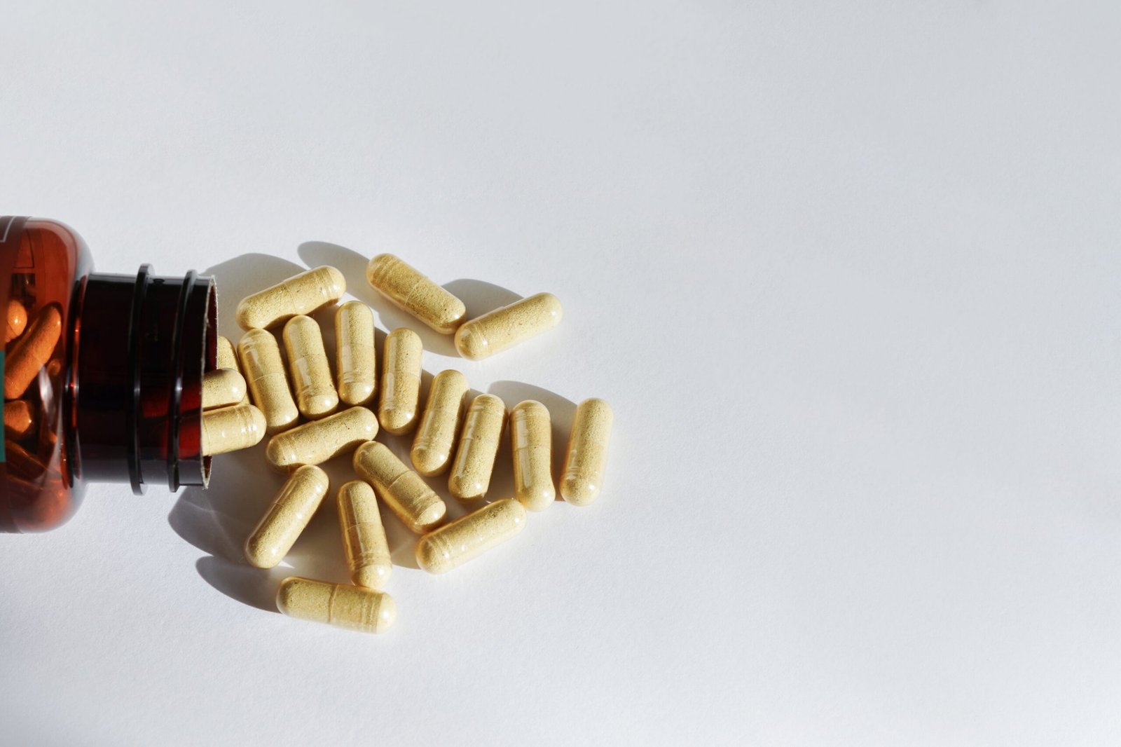A bottle of pills and supplements on it's side with capsules spilling out