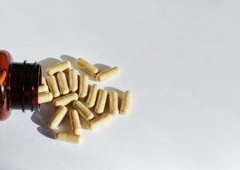 A bottle of pills and supplements on it's side with capsules spilling out